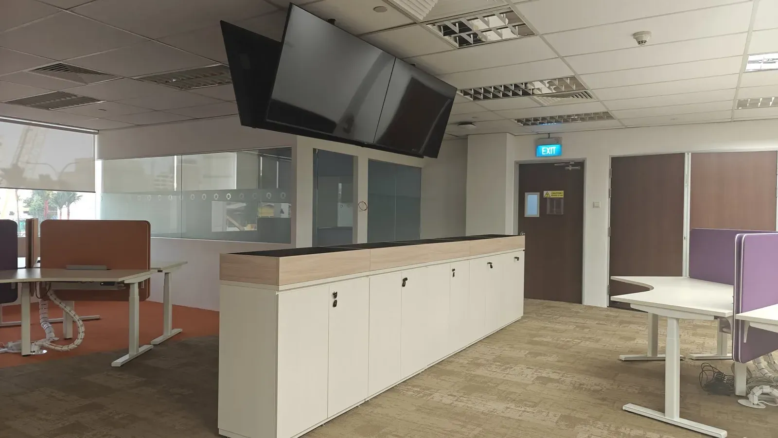 Back-to-back ceiling-hung displays above a storage counter in an open-plan office
