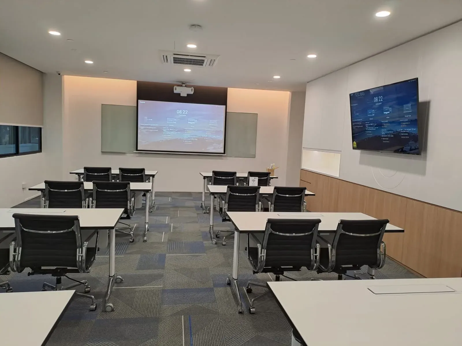 Training room set out in classroom rows, with a projection screen at the front and a wall display at the side, installed by VisionCast